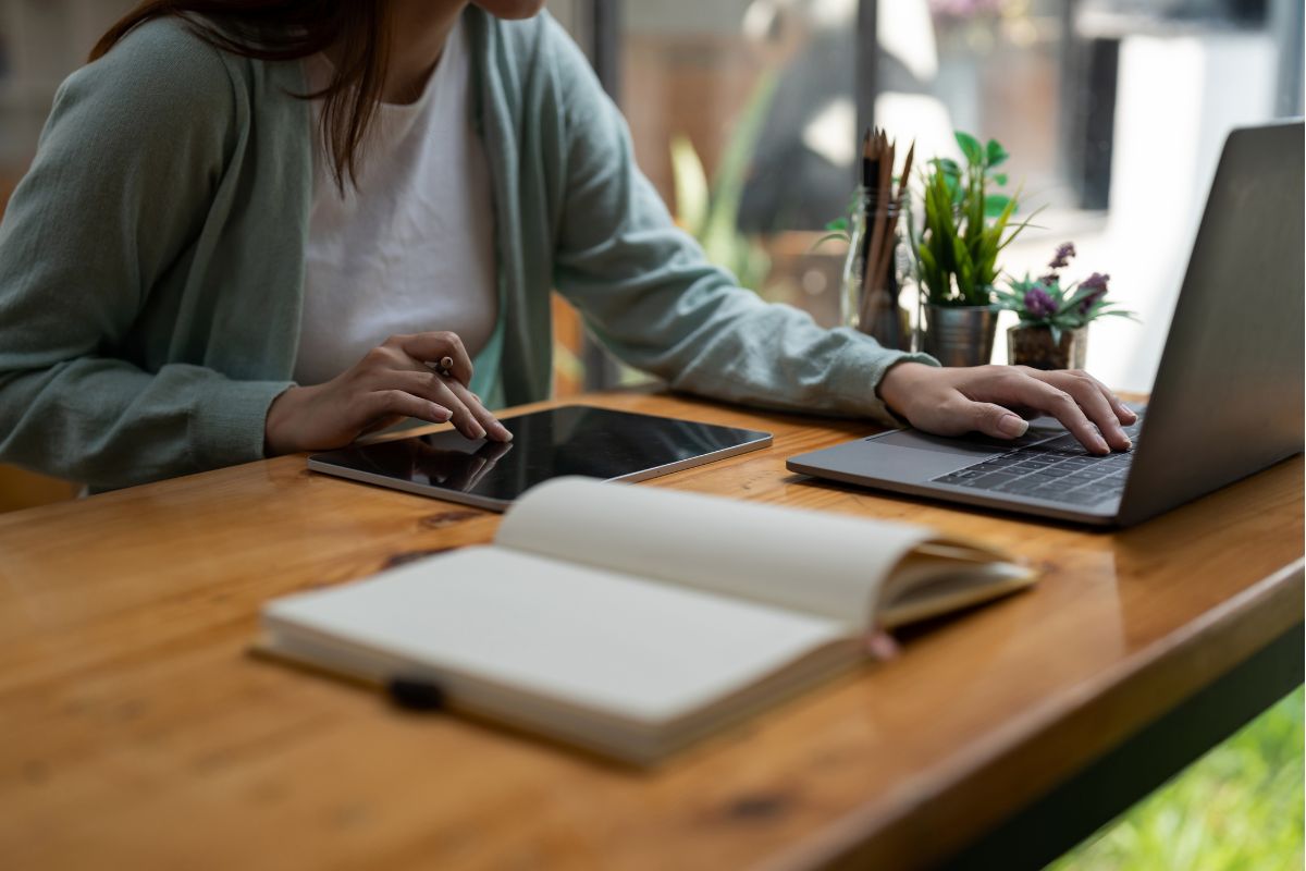 Mulher fechando o caderno de planejamento para começar a construir no laptop — a diferença entre quem planeja e quem constrói